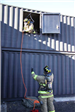 Firefighter in window of training facility rigging for descent via rope