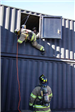 Firefighter descending from training facility window via rope
