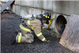Firefighter in gear looking into the entrance of a large pipe in a concrete wall