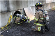Firefighters in gear entering pipe set in concrete wall
