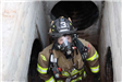 Firefighter in breathing mask and gear inside concrete space with pipe entrances on each side
