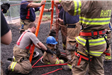 Firefighters lowering a team member into a hole in the ground with safety rigging