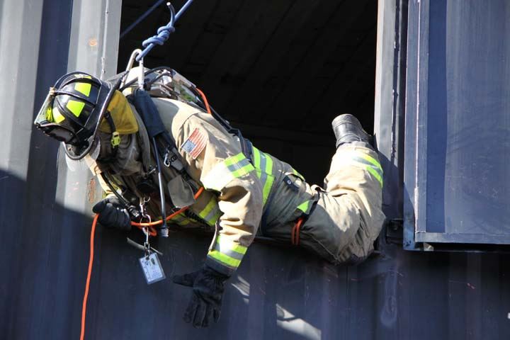 Firefighter descending from window of training facility via rope