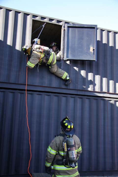 Firefighter descending from training facility window via rope