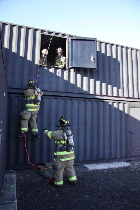 Firefighter descending from training facility window via rope