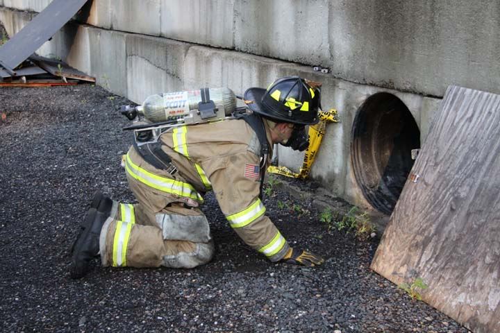 Firefighter in gear looking into the entrance of a large pipe in a concrete wall