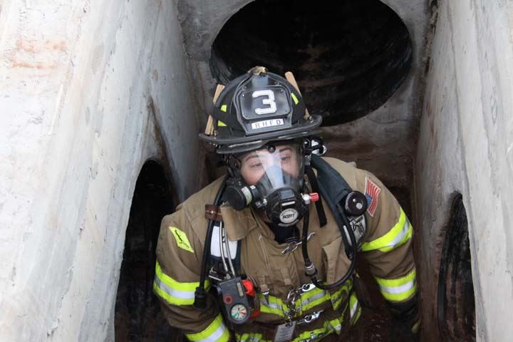 Firefighter in breathing mask and gear inside concrete space with pipe entrances on each side