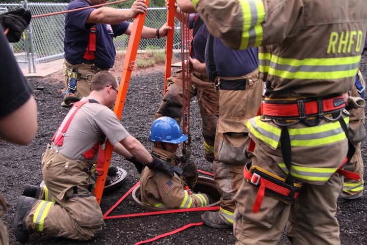 Firefighters lowering a team member into a hole in the ground with safety rigging