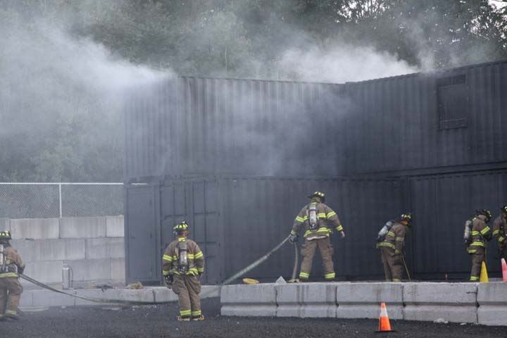 Training facility with smoke coming out and firefighters in gear with hoses training